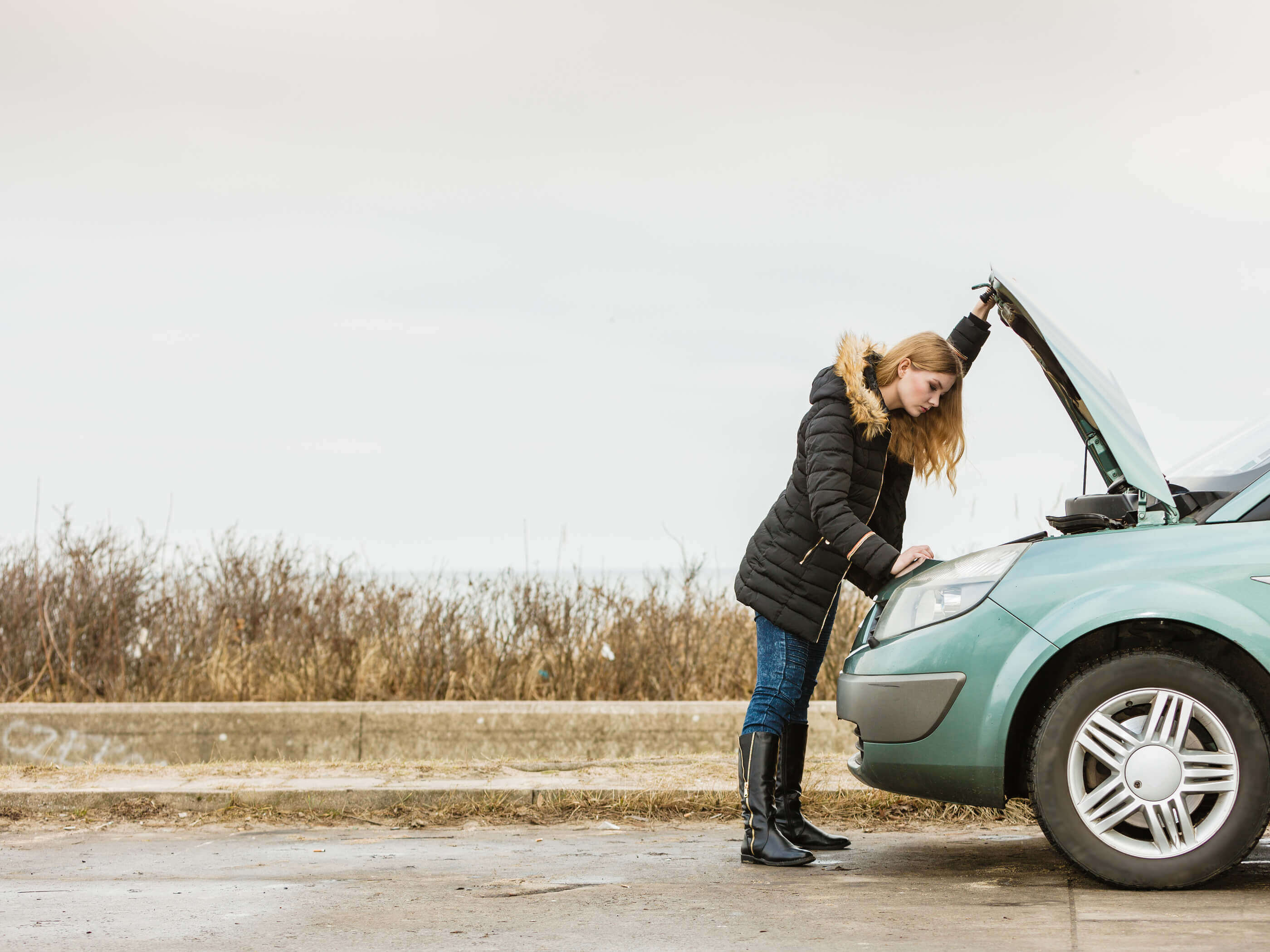 A woman looking at the engine of her broken down car